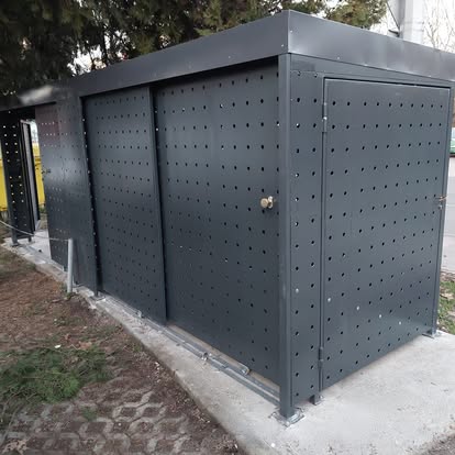 Antracit sivo metalno spremište s perforiranim kliznim vratima na betonskom postolju uz zgradu — Knight Project Zagreb